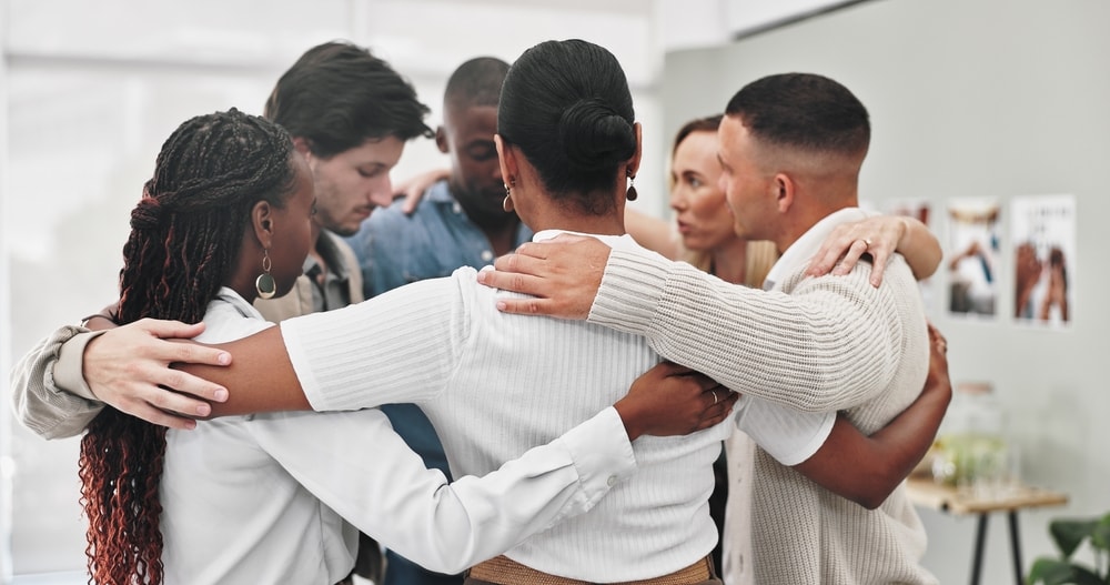 Group therapy, counseling and people hug in rehabilitation center for support, empathy or solidarity. Help, psychology and friends with safety prayer circle for trauma healing, gratitude or thank you